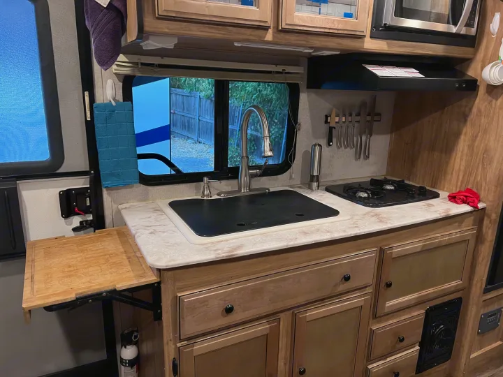 Inside an RV rental, this cozy kitchen features a sink, stove, microwave, cabinets, and a pull-out cutting board.. Coachmen Other 2019