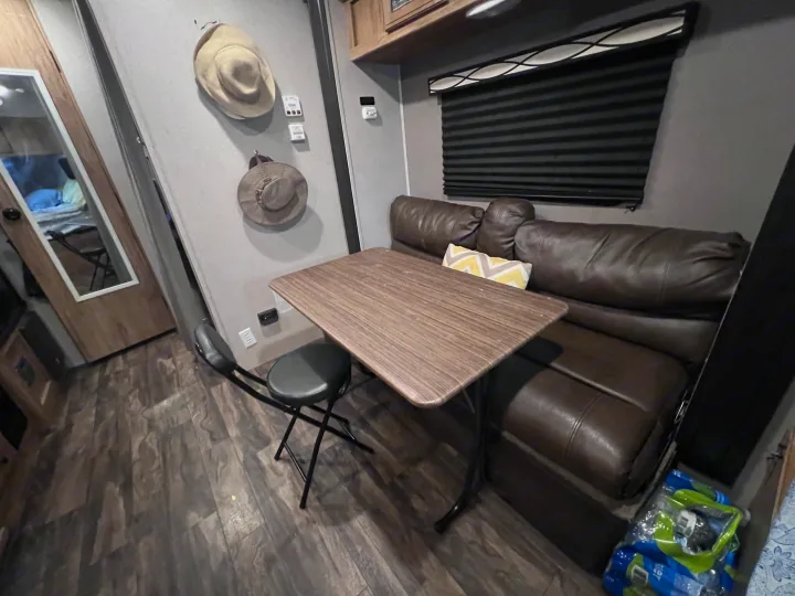 Cozy RV rental interior: A compact dining area with a table and stool, a leather sofa, and window with dark blinds.. Coachmen Other 2019