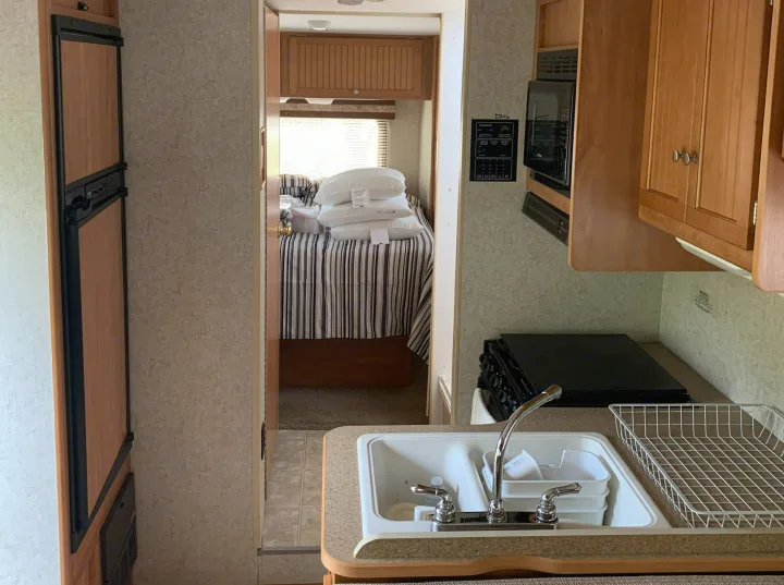 RV rental interior features a compact kitchen with sink, microwave, stove, and fridge, plus a cozy bedroom.. Winnebago Access 2007