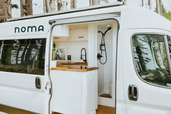 Stylish white rv rental with open side door revealing a modern interior: kitchen, wood counters, and a compact shower.. Ram Promaster 2500 2021