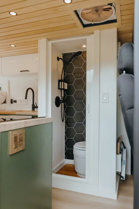 Modern RV rental interior: compact shower/toilet with black hex tiles, wood ceiling, green kitchen. Ready for adventures.. Ram Promaster 2500 2021