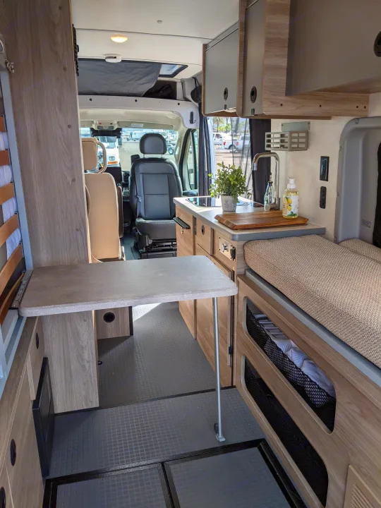 Inside a modern rv rental, featuring a compact kitchen, foldable table, and cozy bed area, looking towards the front.. Winnebago Solis 2023