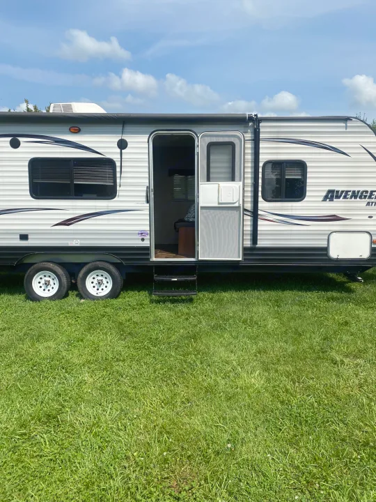 Explore your next adventure with this bright Avenger travel trailer RV rental, parked on vibrant green grass under a blue sky.. Avenger ATI 2015