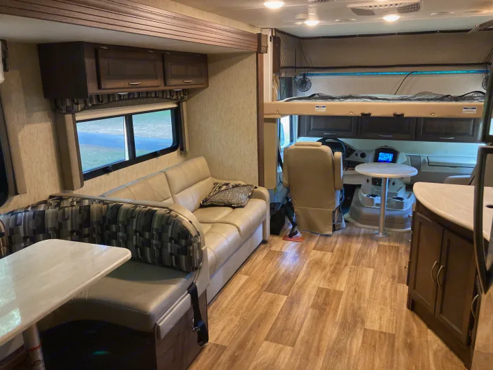 View of a clean RV rental interior, showcasing the dinette, sofa, and driver's area with bunk bed.. Forest River Coachmen Mirada 2019