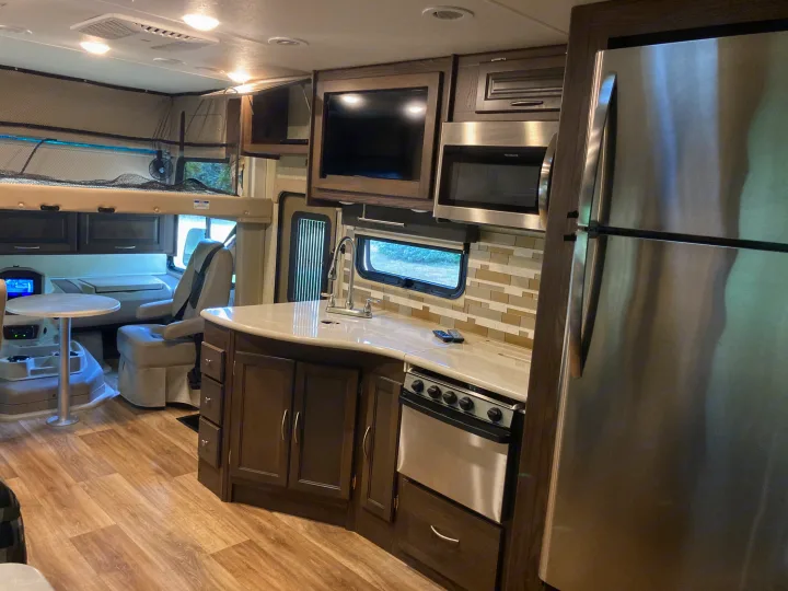Modern RV rental interior showcasing a well-equipped kitchen with stainless appliances, dining area, and overhead bunk.. Forest River Coachmen Mirada 2019