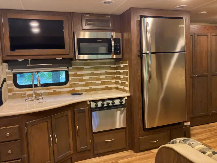 RV rental kitchen: stainless steel fridge, microwave, stove, sink, dark wood cabinets, and tile backsplash. Bright and modern RV interior.. Forest River Coachmen Mirada 2019