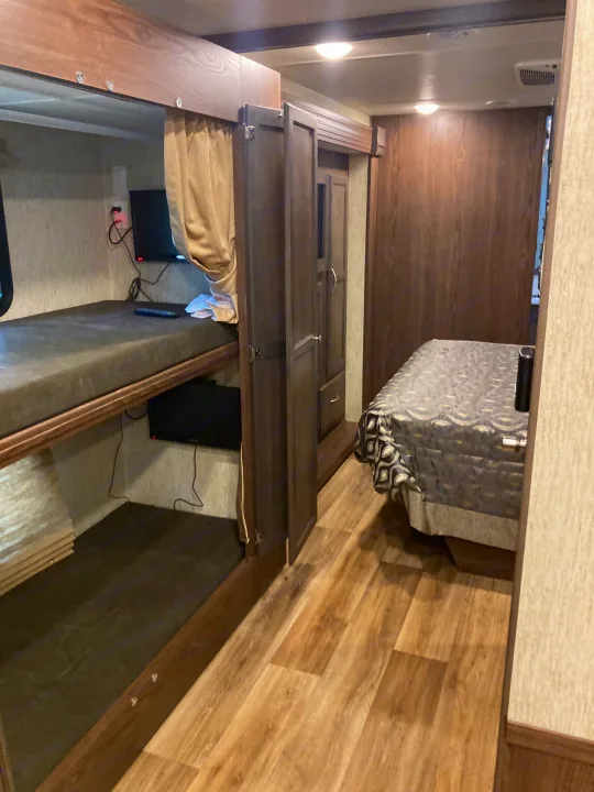 This RV rental interior showcases cozy bunk beds, a practical wardrobe, and a comfy main bedroom area for travel.. Forest River Coachmen Mirada 2019