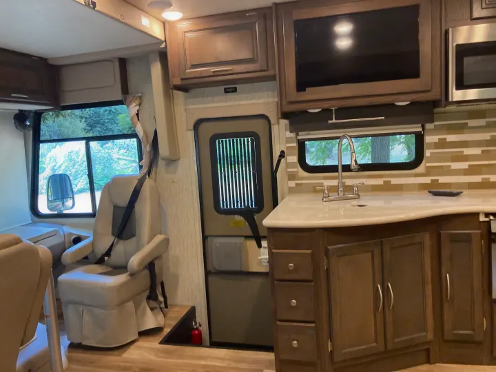 RV rental interior: cozy kitchen with sink, microwave, and swiveling chairs in a well-lit living area.. Forest River Coachmen Mirada 2019