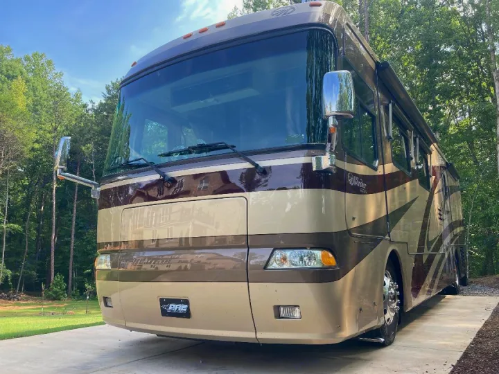Luxury two-tone motorhome for rv rental, parked on a paved pad amidst lush green trees, under clear skies.. Monaco Windsor 2004