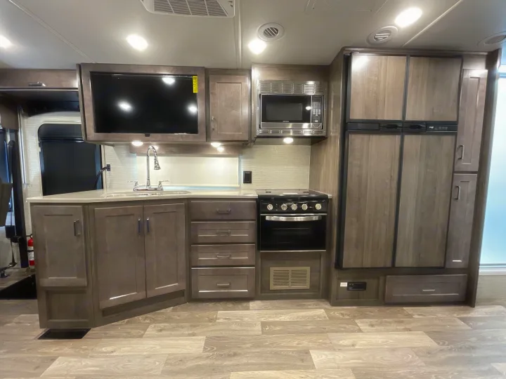 Modern RV rental interior with a fully equipped kitchen: sink, microwave, stove, fridge, ample cabinets, and TV.. Winnebago Sunstar 2022
