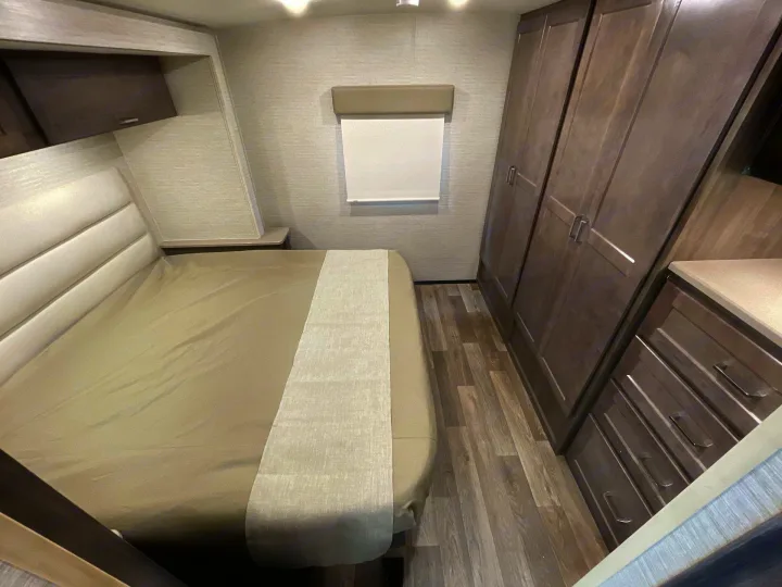 RV rental's cozy bedroom features a bed, modern wood-toned storage cabinets, and a window for comfortable travel.. Winnebago Sunstar 2022