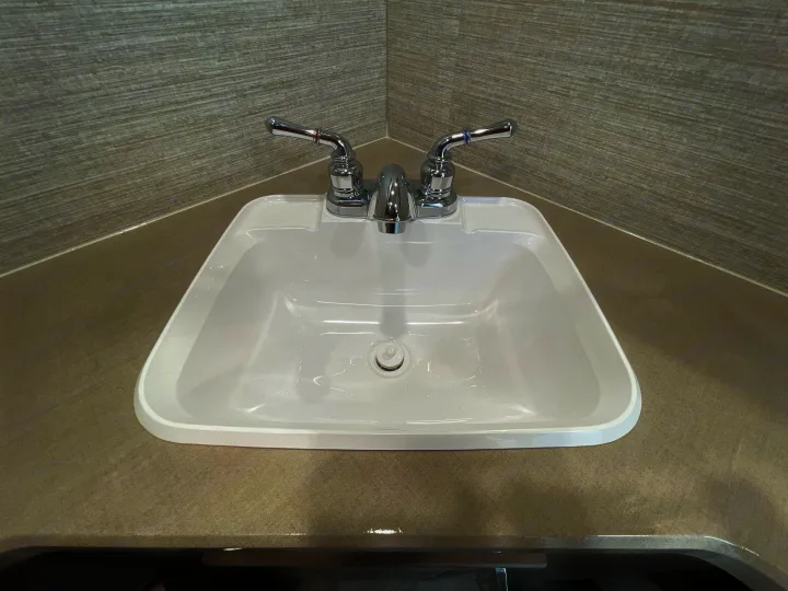 Modern white sink and chrome faucet in a compact RV rental bathroom, featuring a textured corner backsplash.. Winnebago Sunstar 2022