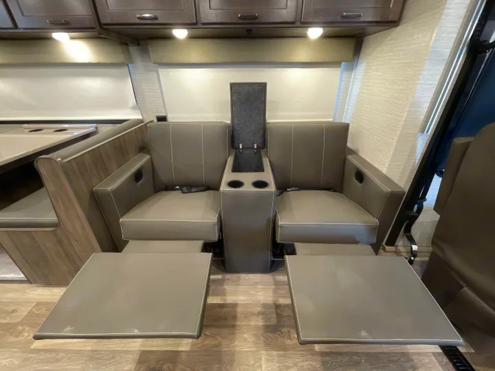 This RV rental interior features two comfy reclining seats with extended footrests, a center console, and overhead cabinets.. Winnebago Sunstar 2022