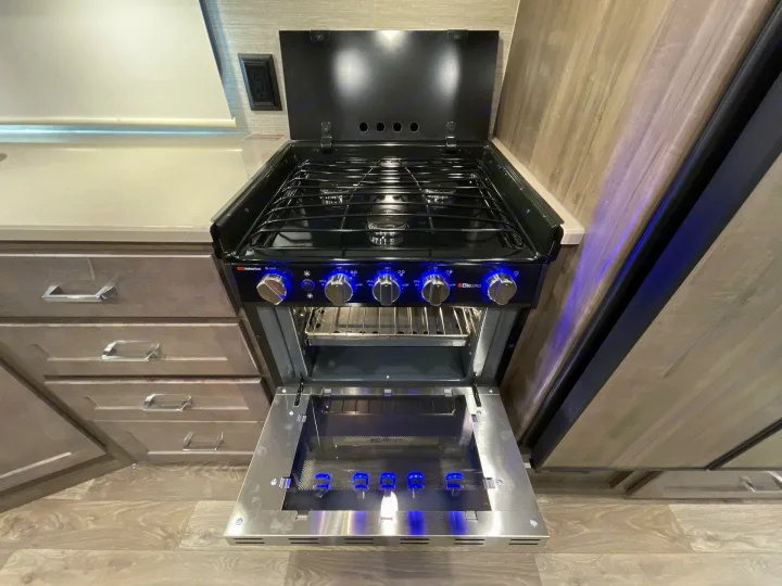 Modern RV rental kitchen with a black gas stove and oven, featuring blue illuminated knobs. Perfect for cooking on the go!. Winnebago Sunstar 2022