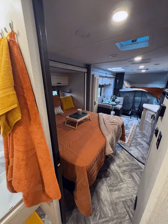 This rv rental features a cozy bedroom with orange bedding, dining area, and bunk beds. Ideal for family travel.. Forest River Sunseeker 2023