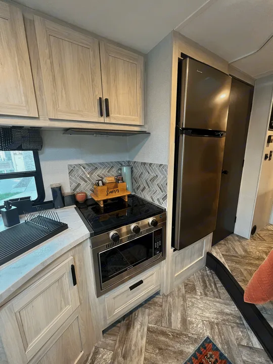 Modern RV rental kitchen featuring light cabinets, stainless steel appliances, and a stylish herringbone backsplash.. Forest River Sunseeker 2023
