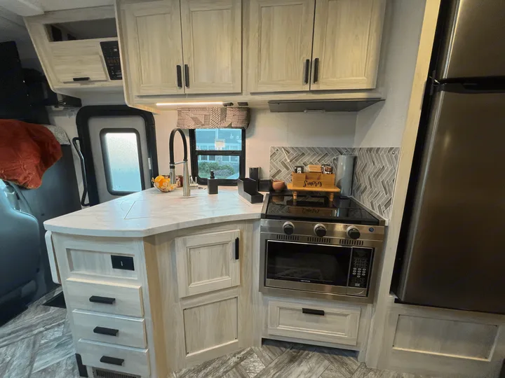 Modern RV rental interior featuring a bright kitchen with light wood cabinetry, full appliances, and a cozy living area.. Forest River Sunseeker 2023