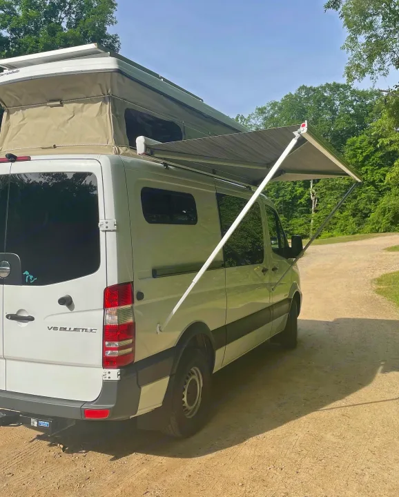 White Mercedes Sprinter RV rental with a pop-top and extended awning on a dirt road, ideal for camping adventures.. Freightliner Sprinter 2015