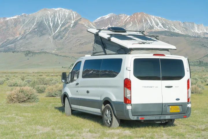 White Ford Transit RV rental van with pop-top & solar panels in snow-capped mountains for outdoor adventure.. Ford transit 2016