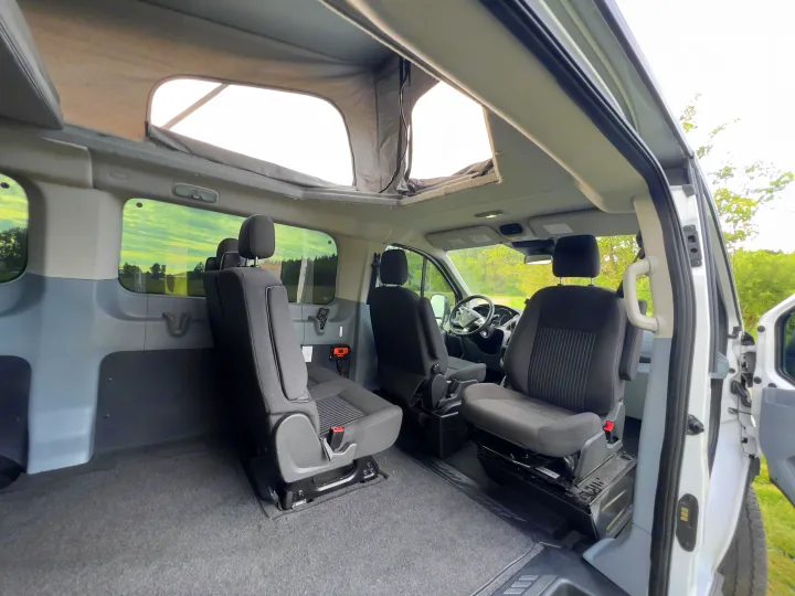 Inside a spacious RV rental van with a pop-top, showing passenger seating and an open rear area.. Ford transit 2016