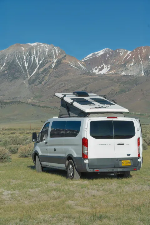 Alaskan RV rental: White Ford Transit van, pop-top deployed, in grassy field with snow-capped mountains.. Ford transit 2016