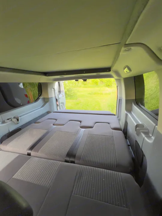 Inside an RV rental: rear seats are flat, forming a bed, looking out to a grassy field. Ideal for travel.. Ford transit 2016