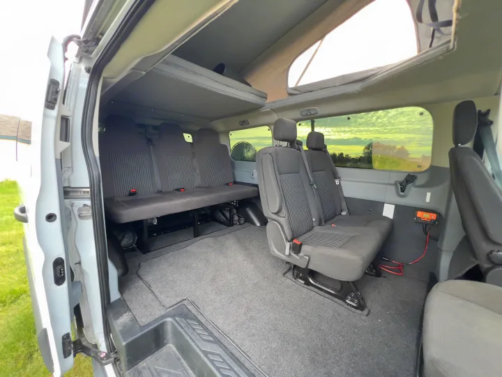 Spacious RV rental interior: pop-top camper van with flexible seating, a convertible bed, & electrical controls.. Ford transit 2016