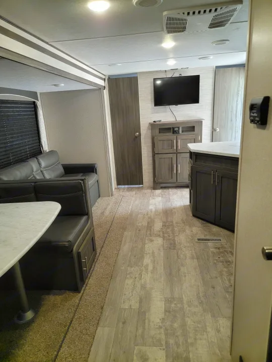 Step inside this RV rental's modern interior: spacious living area with dark wood floors, stylish dark cabinets, cozy seating, and TV.. Forest River Shasta 2019