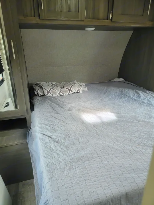 Modern RV rental bedroom: grey quilted bed, patterned blanket, and dark wood cabinets.. Forest River Shasta 2019