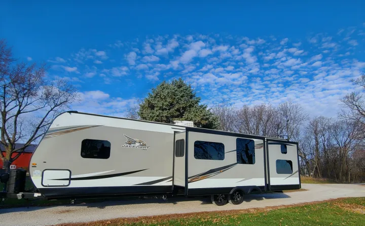 A modern gray and white Jay Flight travel trailer rv rental with slide-outs extended, parked on gravel under a blue sky.. Jayco Jay Flight 2020
