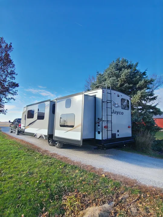 A large Jayco RV rental, hitched to a pickup truck, parked on a gravel drive with extended slide-outs, under a clear sky.. Jayco Jay Flight 2020