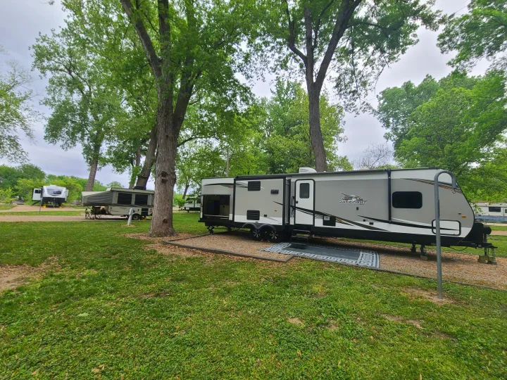 Experience nature with an RV rental! A grey travel trailer and a pop-up camper parked in a green, tree-filled campground.. Jayco Jay Flight 2020