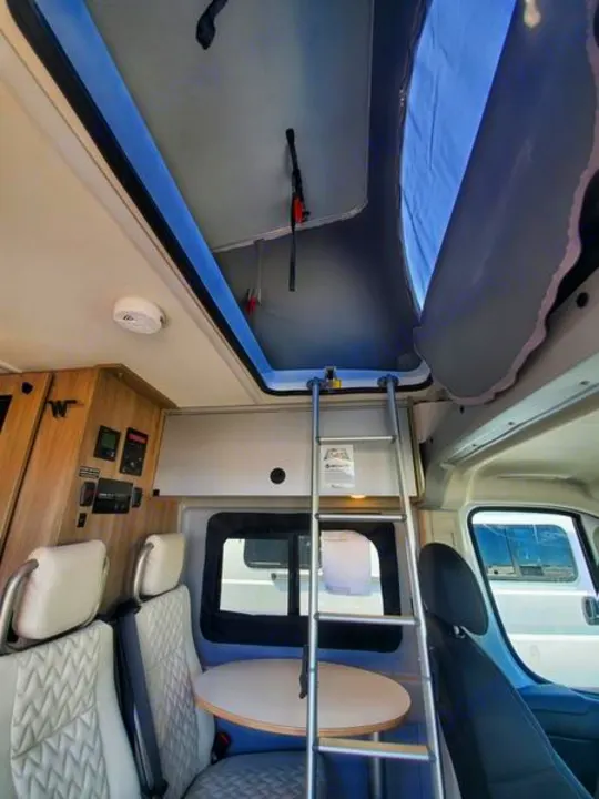 Inside an RV rental: pop-top roof with ladder to bed, swivel seats, and a cozy dinette. Perfect camper van for adventures!. Winnebago Solis 2022