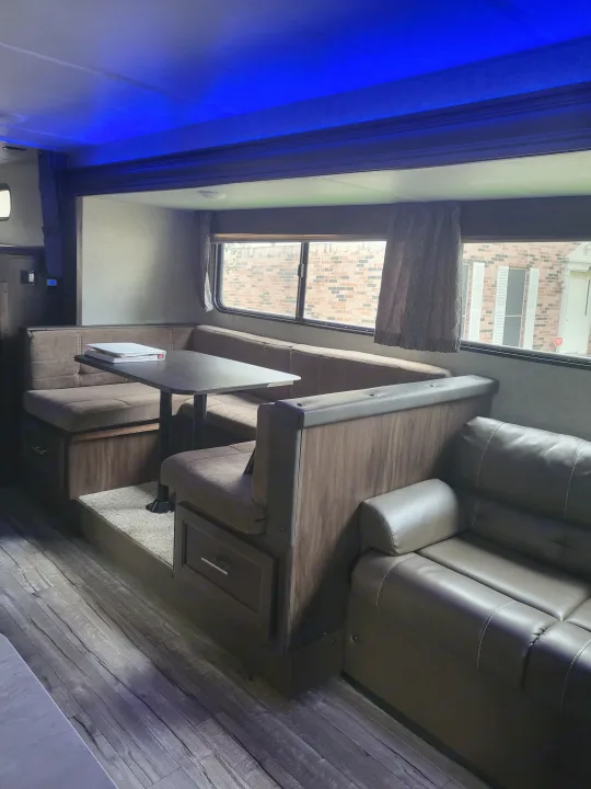 Comfortable RV rental interior showing a brown leather sofa, dinette with table, and blue ambient lighting.. Forest River Cherokee Grey Wolf 2018