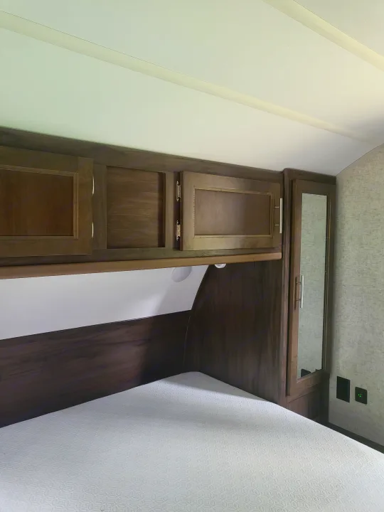 Interior of an RV rental bedroom. Dark wood cabinets, a patterned bed, and overhead mirrored storage maximize space efficiently.. Forest River Cherokee Grey Wolf 2018