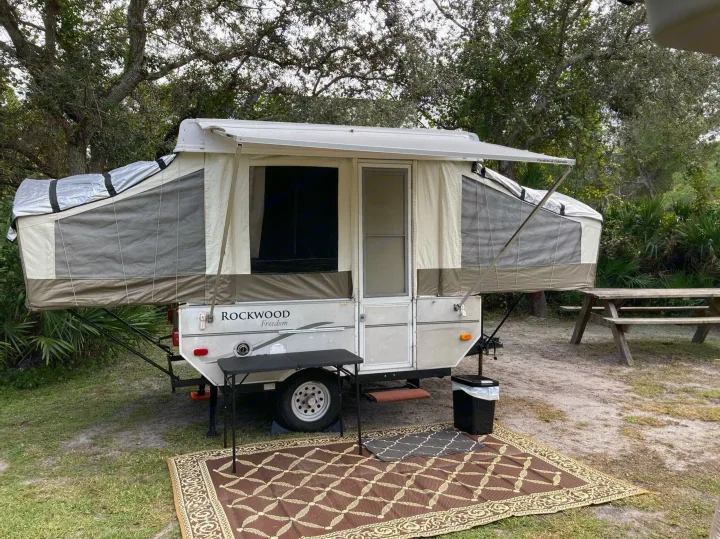 Enjoy this pop-up camper RV rental campsite. Features include an outdoor rug, table, and picnic area among trees.. Forest River Other 2007