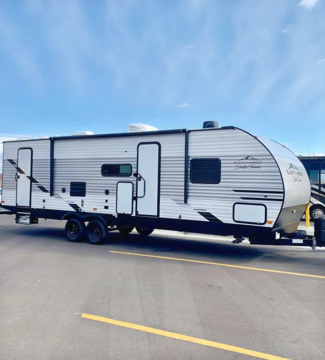 A sleek, gray and white East to West Della Terra travel trailer, an ideal rv rental, parked outdoors under a blue sky.. East to West Other 2022