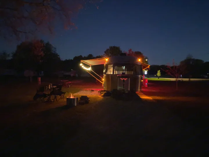 Cozy Airstream RV rental campsite at night with string lights & campfire, perfect for a relaxing outdoor getaway.. Airstream International 2014
