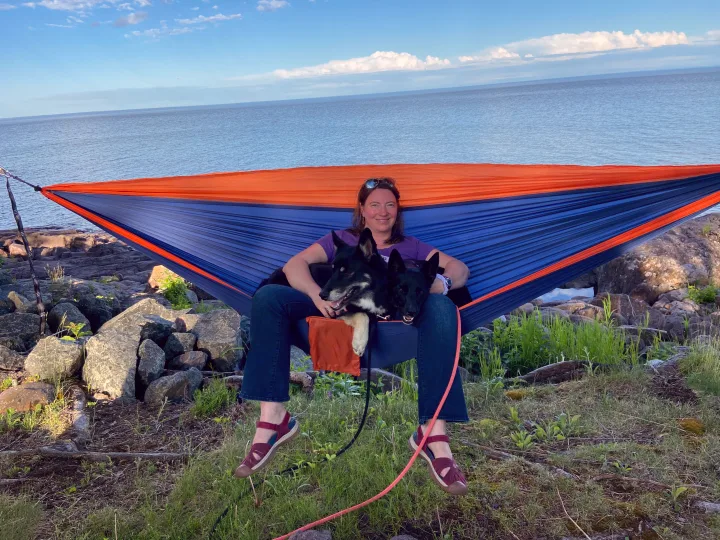 Woman and her two dogs unwinding in a colorful hammock by a vast lake, a scenic stop on an RV rental journey.. Airstream International 2014