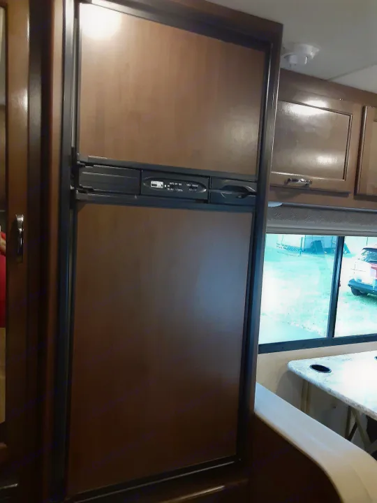 This RV rental features a compact kitchen with a large wood-paneled refrigerator/freezer and cabinets, ideal for a functional living space.. Thor Freedom Elite 2018