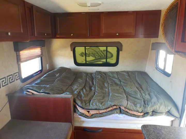 Cozy RV rental interior showing a compact bedroom with sleeping bags, overhead cabinets, and windows.. Clipper Clipper Trailer 2015