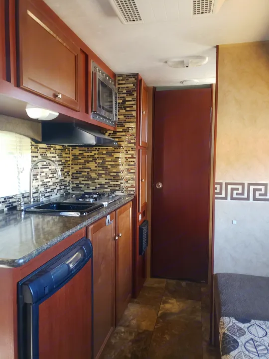 RV rental kitchen showing wood cabinets, sink, microwave, stove, tiled backsplash, and patterned flooring.. Clipper Clipper Trailer 2015