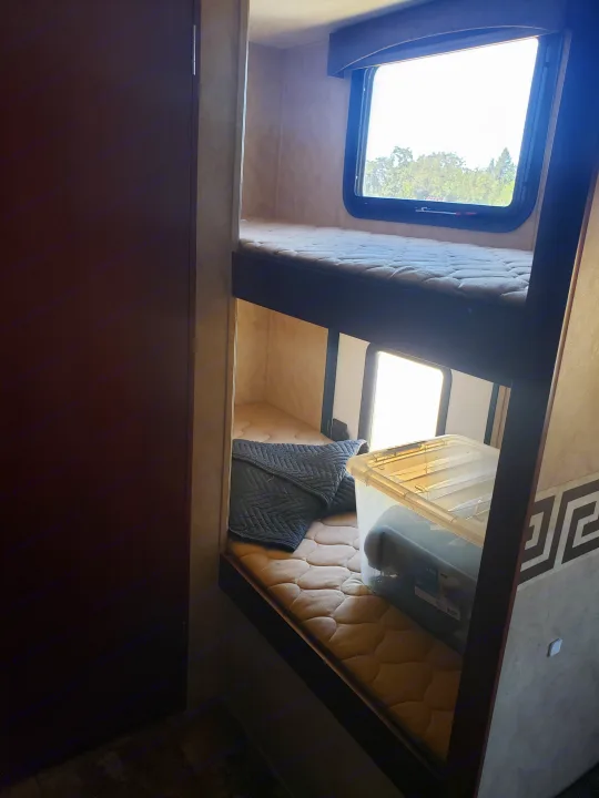 Comfortable bunk beds in an RV rental, complete with a window view of trees, a cozy blanket, and a clear storage bin.. Clipper Clipper Trailer 2015