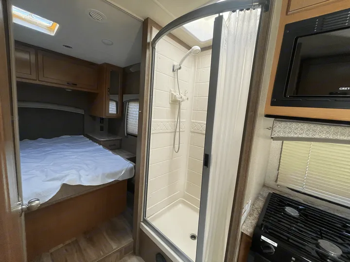 Inside this RV rental: a compact shower, bed, and kitchen area with microwave/stove, offering all essentials for travel.. Thor Four Winds 2021