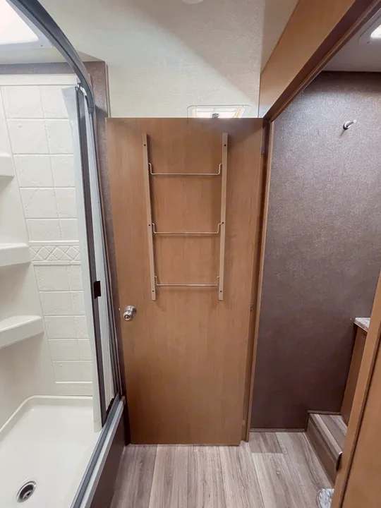 Inside an RV rental: View of a compact bathroom featuring a shower, wooden door with towel rack, and laminate floor.. Thor Four Winds 2021