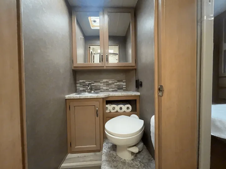 Inside an RV rental bathroom: sink, vanity, mirrored medicine cabinet, toilet, and toilet paper storage.. Thor Four Winds 2021
