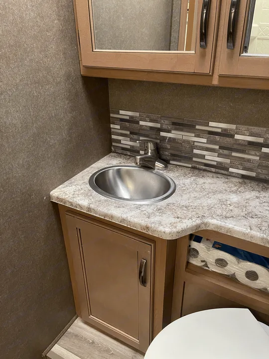 Essential RV rental bathroom setup: compact vanity with stainless steel sink, mirror, and accessible toilet paper storage.. Thor Four Winds 2021