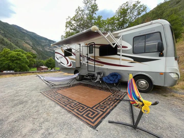 Relaxing RV rental setup in a scenic mountain campground with two hammocks, chairs, and an outdoor mat.. Fleetwood Storm 32BH 2013