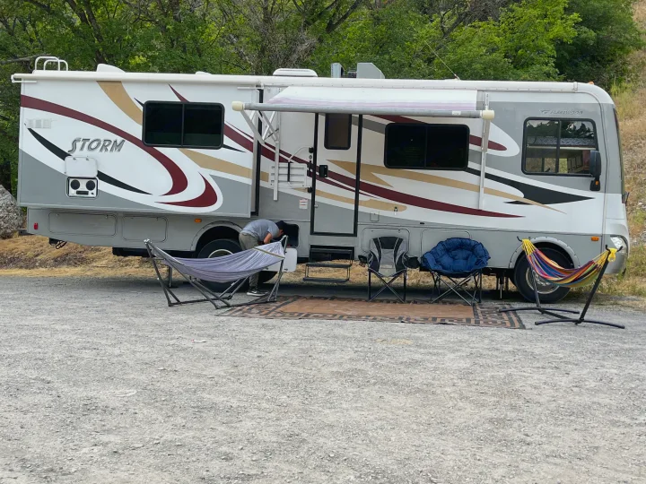 RV rental ready for adventure: A Fleetwood Storm motorhome with awnings, hammocks, & camp chairs set up at a gravel campsite.. Fleetwood Storm 32BH 2013