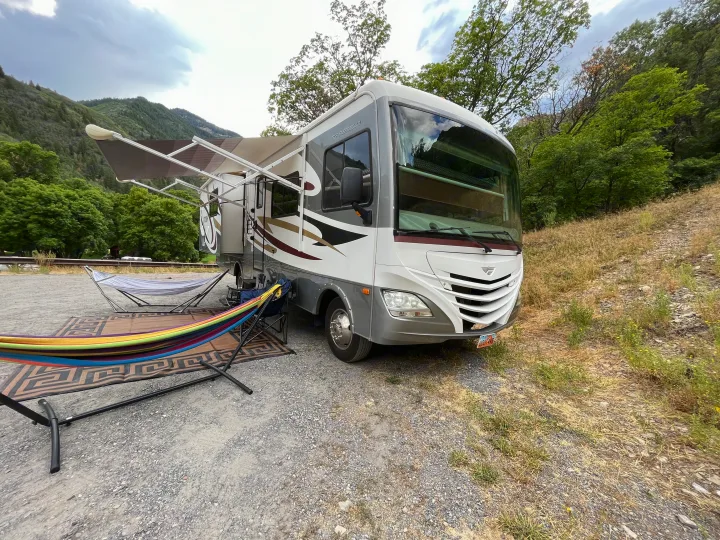 RV rental parked in a scenic mountain setting, with vibrant hammocks and an outdoor rug ready for relaxation.. Fleetwood Storm 32BH 2013